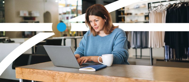 A woman seated at a table, focused on her laptop, engaged in work or study.